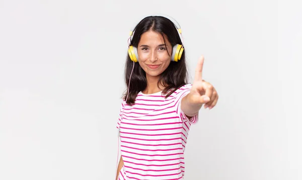 若いヒスパニック系の女性は誇らしげに笑顔で自信を持ってヘッドフォンでナンバーワンのリスニング音楽を作ります — ストック写真