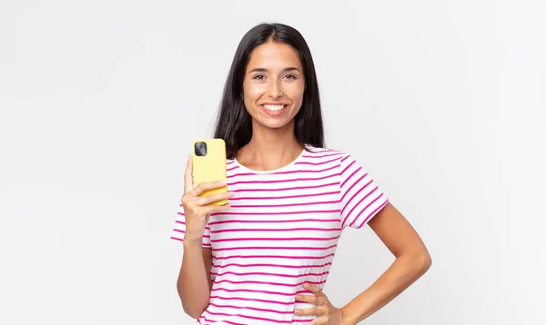 Młoda Latynoska Uśmiechnięta Szczęśliwie Ręką Biodrze Pewna Siebie Trzymająca Smartfona — Zdjęcie stockowe