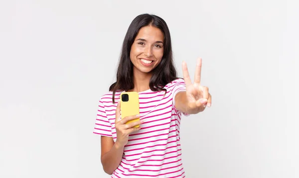 Молодая Латиноамериканка Улыбается Выглядит Дружелюбно Показывая Номер Два Держа Смартфон — стоковое фото