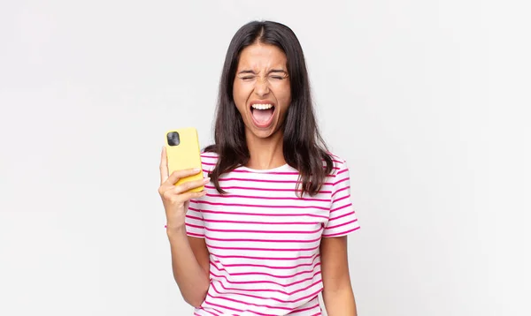 若いヒスパニック系の女性が積極的に叫びとても怒ってスマートフォンを持っています — ストック写真