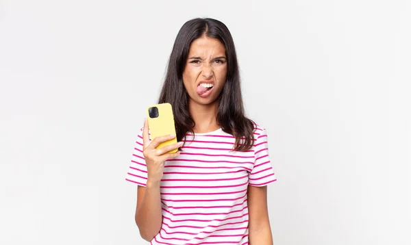 Jovem Hispânica Sentindo Enojado Irritado Língua Para Fora Segurando Smartphone — Fotografia de Stock