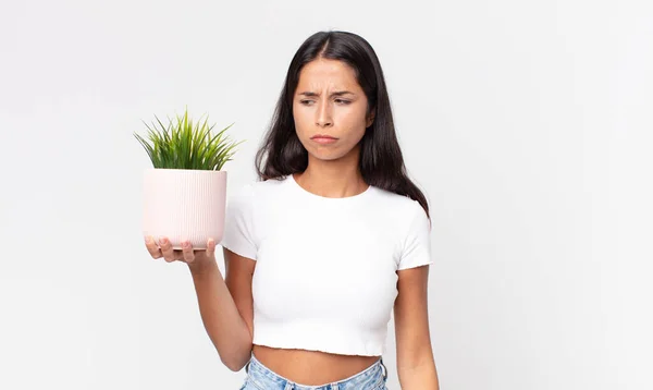 若いヒスパニック系の女性は悲しい 動揺や怒りを感じ 側面を見て 装飾的な家の植物を保持します — ストック写真