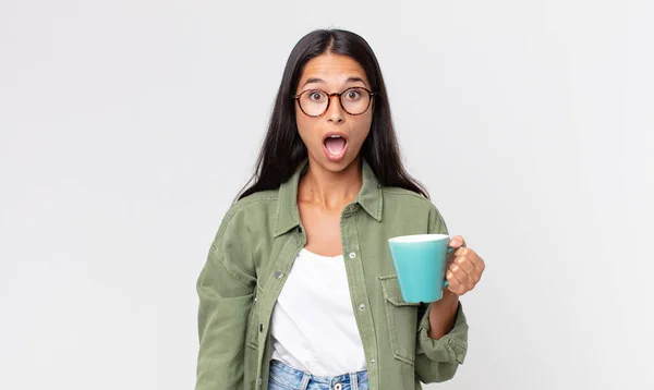 若いヒスパニック系の女性がショックを受けたり驚いたりコーヒーマグカップを持っていて — ストック写真