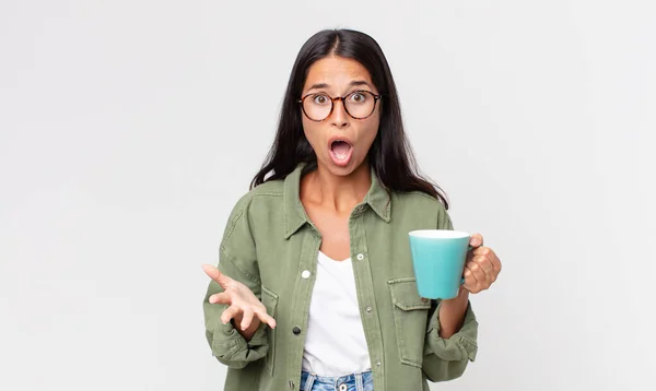 若いヒスパニック系の女性はとてもショックを受け驚きコーヒーマグカップを持っています — ストック写真