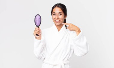 Bornoz giymiş ve elinde saç fırçası tutan güzel İspanyol bir kadın.