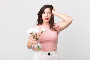 Güzel bir kadın stresli, endişeli ya da korkmuş hissediyor, elleri başının üstünde ve elinde dekoratif bir saksı tutuyor.