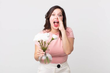 Güzel bir kadın kendini mutlu hissediyor, elleri ağızının yanında ve elinde dekoratif bir saksıyla bağırıyor.