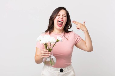 Güzel bir kadın mutsuz ve stresli görünüyor, intihar jesti silah işareti yapıyor ve elinde dekoratif bir saksı tutuyor.