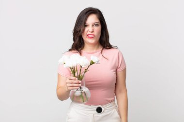 Güzel bir kadın şaşkın ve şaşkın görünüyor ve elinde dekoratif bir saksı tutuyor.