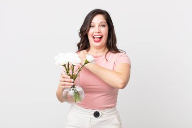 Güzel bir kadın kendini mutlu hisseder ve meydan okumayla yüzleşir ya da kutlama yapar ve elinde dekoratif bir saksı taşır.