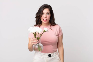 Güzel bir kadın şaşkın ve şaşkın hissediyor ve elinde dekoratif bir saksı tutuyor.