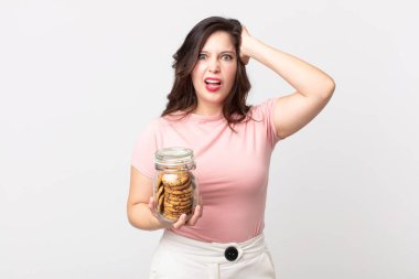 Güzel bir kadın stresli, endişeli ya da korkmuş hissediyor. Elleri başının üstünde ve elinde cam bir kurabiye şişesi tutuyor.