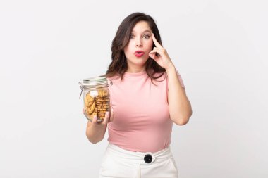 Güzel kadın şaşırmış görünüyor, yeni bir düşünce, fikir ya da konsept fark ediyor ve elinde cam bir kurabiye şişesi tutuyor.