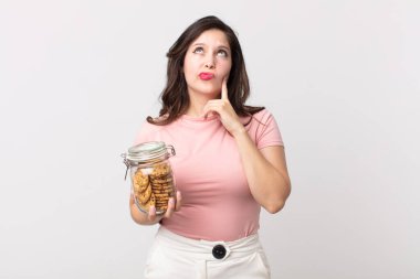 Güzel bir kadın düşünüyor, kuşkulu ve şaşkın hissediyor ve elinde cam bir kurabiye şişesi tutuyor.