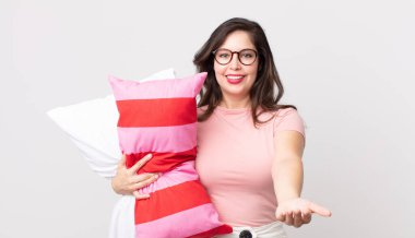 Güzel bir kadın mutlu bir şekilde gülümsüyor ve pijama giyip yastık tutuyor.