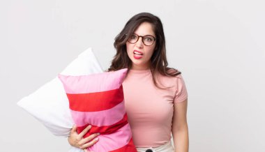 Güzel bir kadın şaşkın ve kafası karışmış hissediyor pijama giyiyor ve yastık tutuyor.