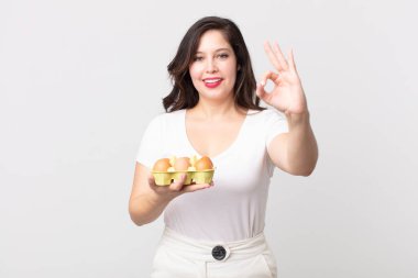 Güzel bir kadın kendini mutlu hissediyor. Onaylıyor. Güzel bir jest ve yumurta kutusu tutuyor.