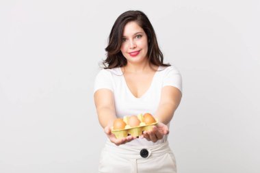 Güzel bir kadın mutlu bir şekilde gülümsüyor ve bir konsept sunuyor ve bir yumurta kutusu tutuyor.