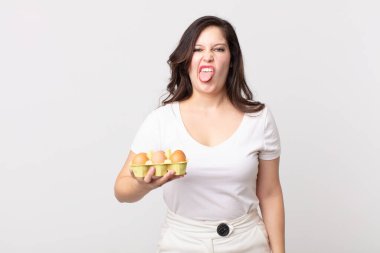 Güzel bir kadın midesi bulanmış ve tedirgin olmuş hissediyor. Dilini çıkarmış ve elinde bir yumurta kutusu tutuyor.