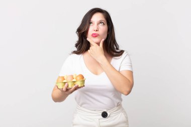 Düşünen, kuşkulu, kafası karışık ve elinde bir yumurta kutusu tutan güzel bir kadın.