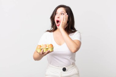 Güzel bir kadın mutlu, heyecanlı ve şaşırmış ve elinde bir yumurta kutusu tutuyor.