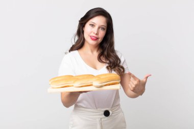 Güzel bir kadın neşeyle gülümsüyor, mutlu hissediyor ve bir tarafı işaret ediyor ve elinde bir ekmek tepsisi tutuyor.