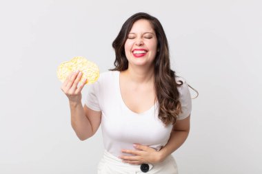 Güzel bir kadın komik bir şakaya yüksek sesle gülüyor ve elinde diyet pirinç keki tutuyor.