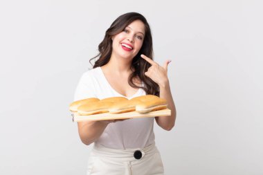 Güzel bir kadın kendi gülüşünü ve ekmek tepsisini göstererek güvenle gülümsüyor.