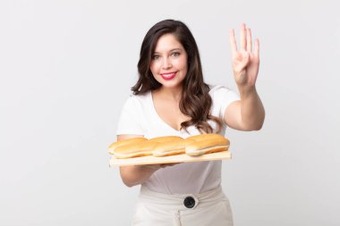 Güzel bir kadın gülümsüyor ve arkadaş canlısı görünüyor, dört numarayı gösteriyor ve elinde bir ekmek tepsisi tutuyor.