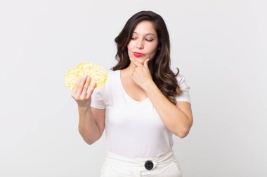 Güzel bir kadın mutlu ve kendinden emin bir ifadeyle gülümsüyor. Elleri çenesinde ve elinde diyet pirinç keki tutuyor.