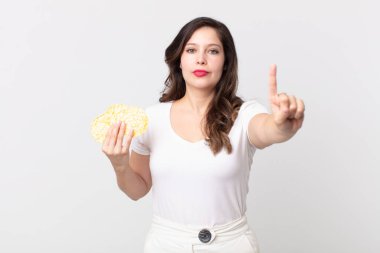 Güzel bir kadın gülümsüyor ve arkadaş canlısı görünüyor. Bir numarayı gösteriyor ve elinde diyet pirinç keki tutuyor.