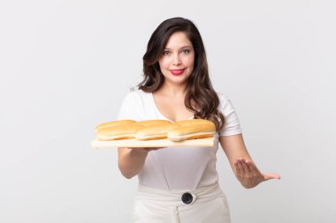 Güzel bir kadın neşeyle gülümsüyor, mutlu hissediyor ve bir konsept gösteriyor ve elinde bir ekmek tepsisi tutuyor.