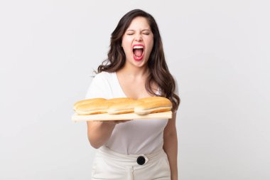 Güzel bir kadın agresif bir şekilde bağırıyor, kızgın görünüyor ve elinde ekmek tepsisi tutuyor.