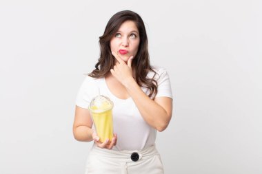 Güzel bir kadın düşünüyor, kuşkulu ve şaşkın hissediyor ve elinde vanilyalı milkshake tutuyor.