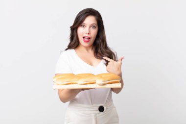 Güzel bir kadın kendini mutlu hissediyor ve heyecanlı ve elinde ekmek tepsisiyle kendini işaret ediyor.