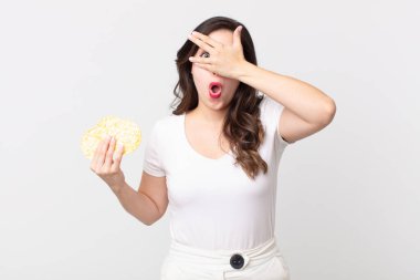 Güzel bir kadın şok olmuş, korkmuş ya da korkmuş görünüyor. Yüzü elle kaplanmış ve elinde diyet pirinç keki tutuyor.