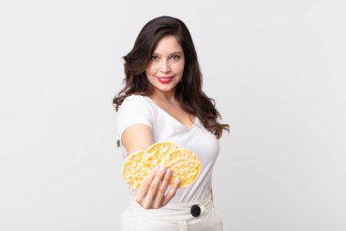 Güzel bir kadın mutlu bir şekilde gülümsüyor ve bir konsept sunuyor ve elinde diyet pirinç keki tutuyor.