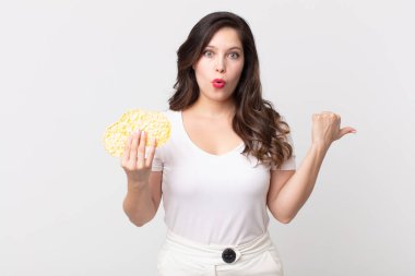 Güzel bir kadın inançsızlığa şaşırmış görünüyor ve elinde diyet pirinç keki tutuyor.