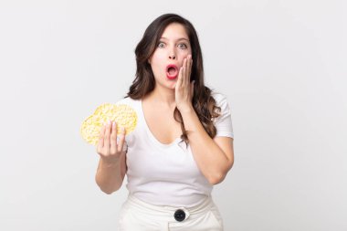 Güzel bir kadın şok olmuş ve korkmuş hissediyor ve elinde diyet pirinç keki tutuyor.