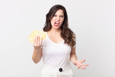 Güzel bir kadın kızgın, sinirli ve hayal kırıklığına uğramış görünüyor ve elinde diyet pirinç keki tutuyor.