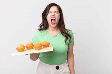 Güzel bir kadın agresif bir şekilde bağırıyor, çok kızgın görünüyor ve elinde kek tepsisi var.