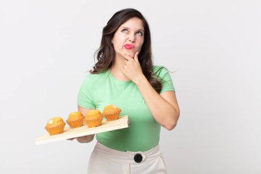 Güzel bir kadın düşünüyor, kuşkulu ve şaşkın hissediyor ve elinde kek tepsisi tutuyor.