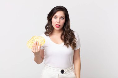 Güzel bir kadın şaşkın ve şaşkın hissediyor ve elinde diyet pirinç keki tutuyor.