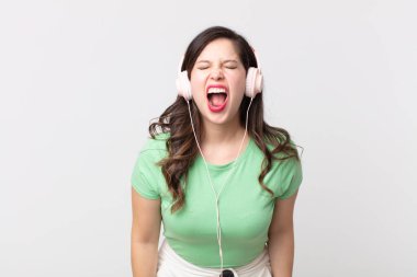 Güzel bir kadın agresif bir şekilde bağırıyor, çok kızgın görünüyor kulaklıkla müzik dinliyor.