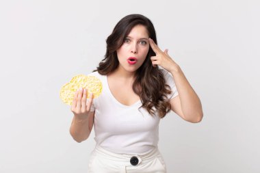 Güzel kadın şaşırmış görünüyor, yeni bir düşünce, fikir ya da konsept fark ediyor ve elinde diyet pirinç keki tutuyor.