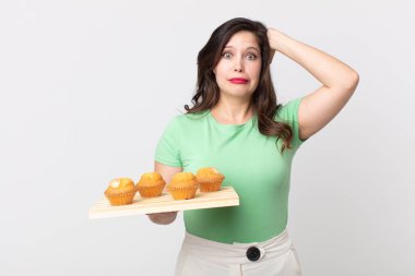 Güzel bir kadın kendini stresli, endişeli ya da korkmuş hissediyor. Elleri başının üstünde ve elinde kek tepsisi var.