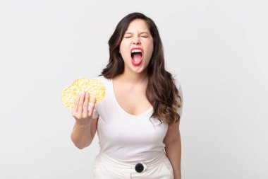 Güzel bir kadın agresif bir şekilde bağırıyor, çok kızgın görünüyor ve elinde diyet pirinç keki tutuyor.