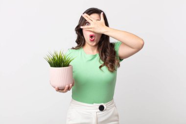 Güzel bir kadın şok olmuş, korkmuş ya da korkmuş görünüyor. Yüzü elle kaplanmış ve elinde dekoratif bir bitki tutuyor.