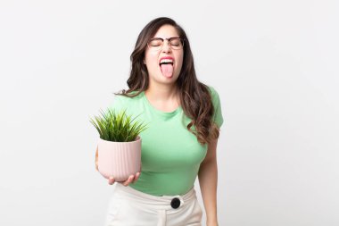 Neşeli ve asi tavırlı güzel bir kadın, şaka yapıyor, dilini dışarı çıkarıyor ve elinde dekoratif bir bitki tutuyor.