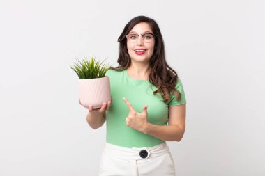 Güzel bir kadın neşeyle gülümsüyor, mutlu hissediyor ve bir tarafı işaret ediyor ve elinde dekoratif bir bitki tutuyor.